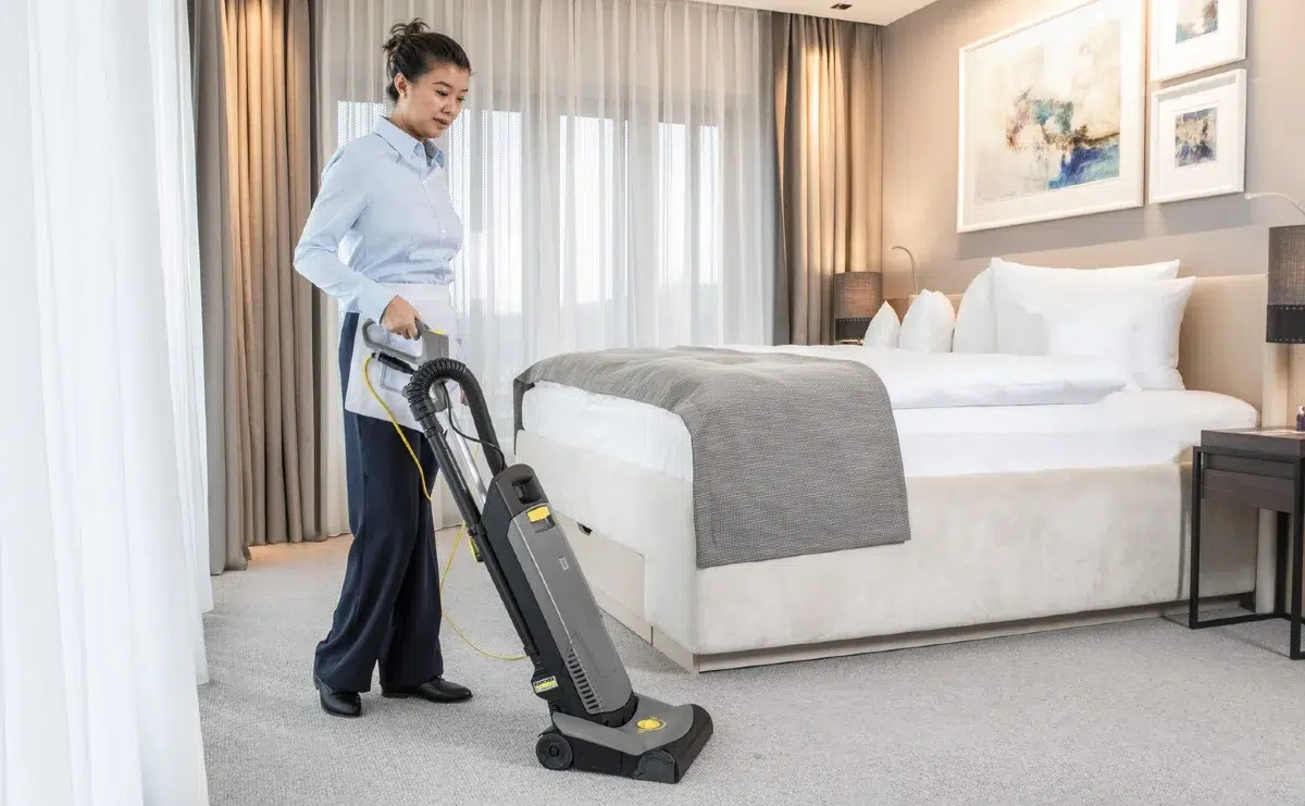 Femme de chambre Nova Hélios en tenue professionnelle dressant un lit dans une suite d'hôtel parisien haut de gamme
